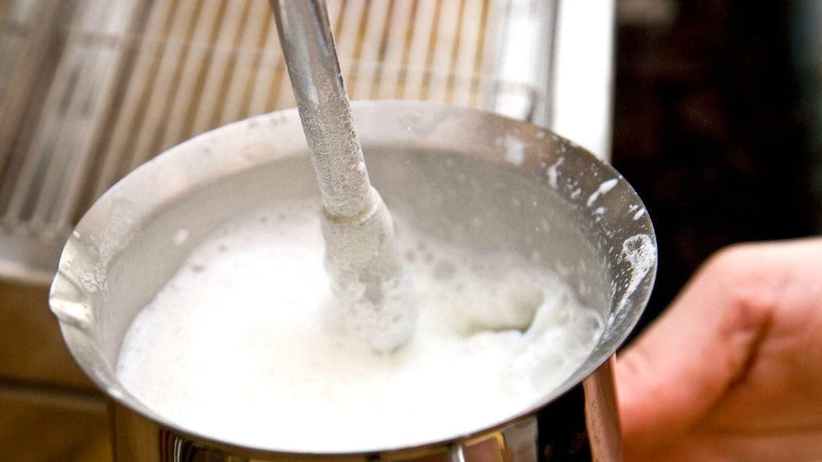 A stainless steel jug with a steam wand frothing milk