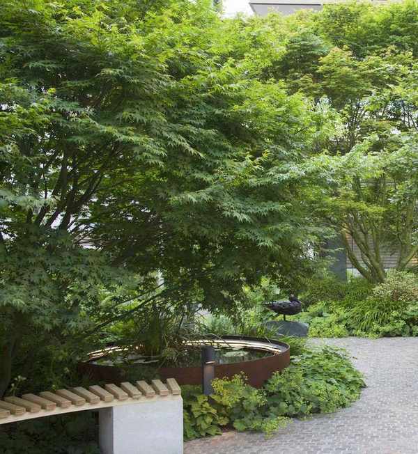 Paved seating area in a shady garden with lush, green planting