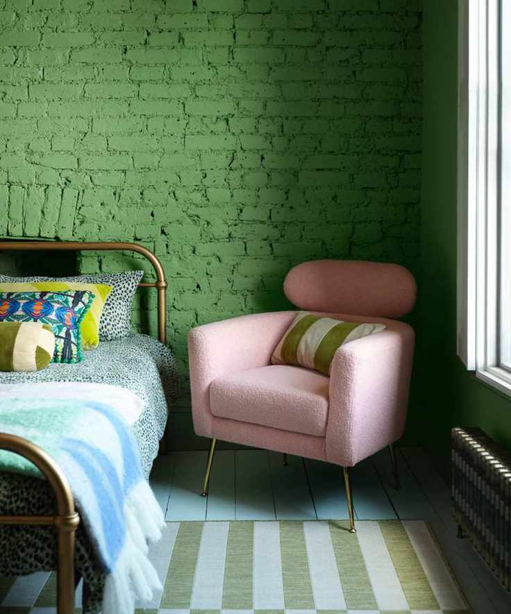 Green painted brick wall in bedroom with striped rug and pink accent chair