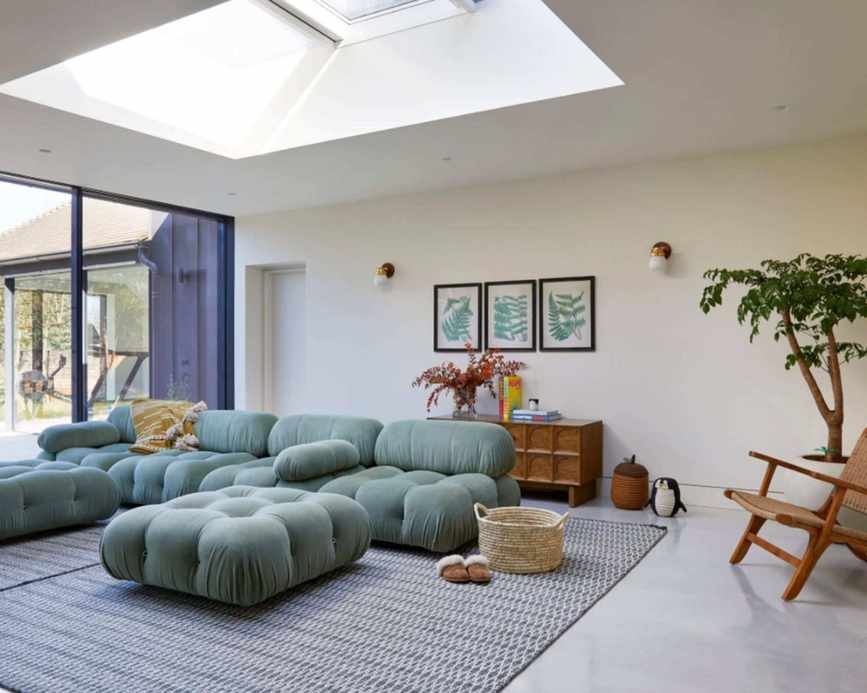A large open plan sitting room with white walls and white ceiling, with bi-fold doors and a large green modern sofa