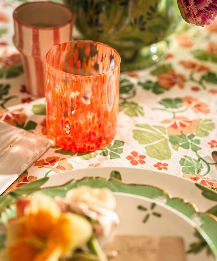 A focused shot of a bright orange speckled glass on a floral tablecloth