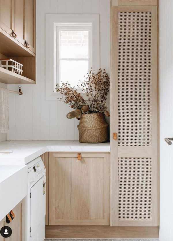 Neutral laundry room with natural wood cabinets and decorative flowers.