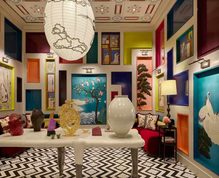 An eclectic room with colorful, recessed display niches showcasing art, bold black-and-white chevron flooring, unique sculptures, and a large paper lantern.