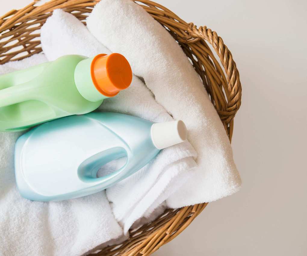 A laundry basket with folded sheets and laundry detergent bottles