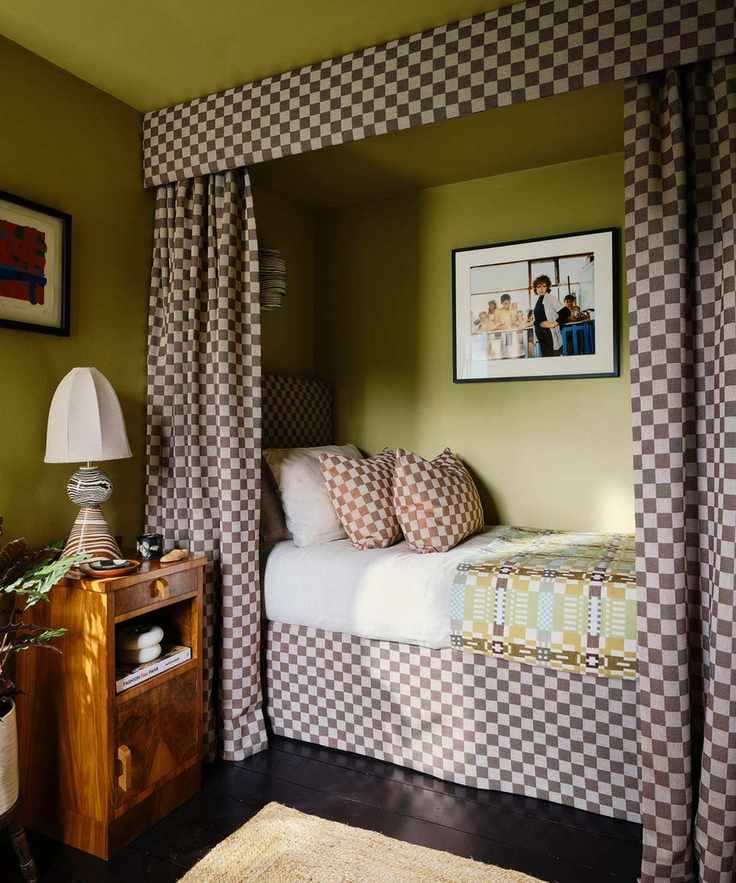 green bedroom with a built in canopy bed nook with checkerboard drapes, bed skirt, and matching throw pillows decorated with vintage furniture and decor
