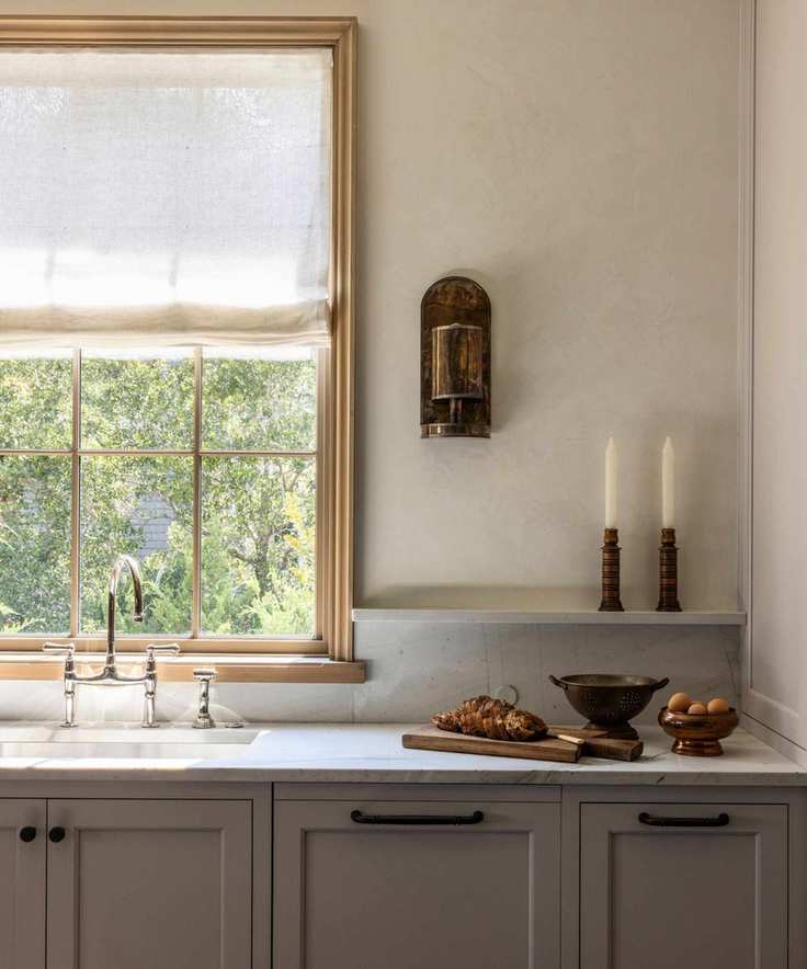 A small kitchen with deep taupe cabinets, marble countertops, and a warm white textured wall paint