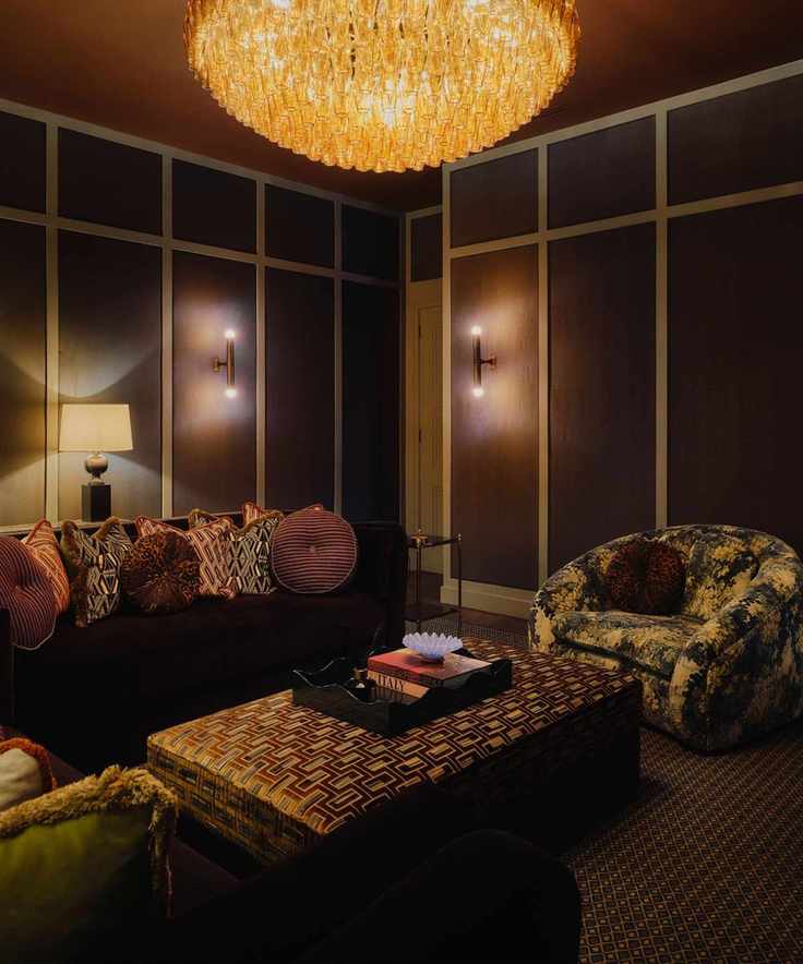 moody dark brown red media room with a dark patterned carpet, printed ottoman and armchairs and a sofa with retro style cushions