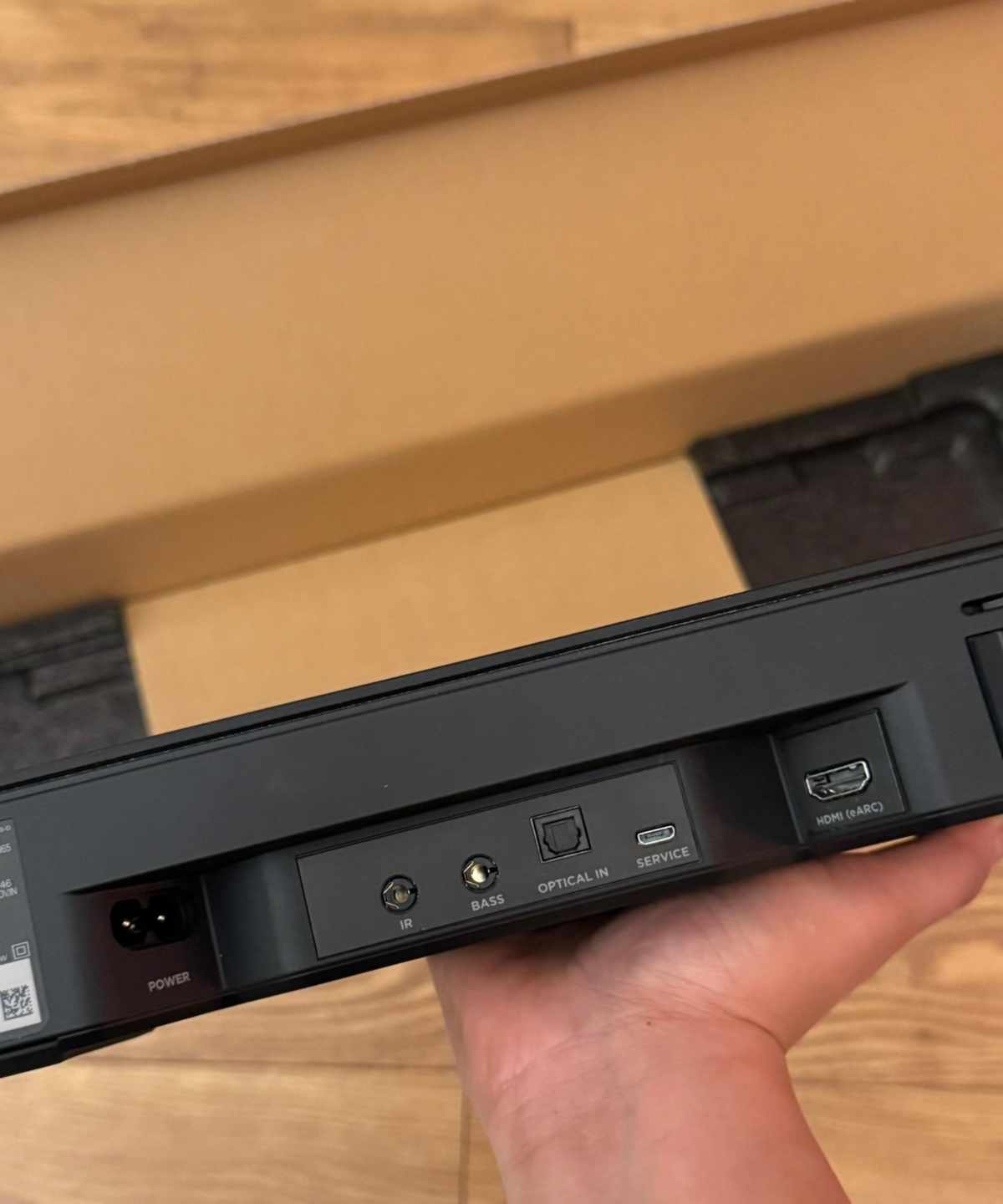 Bose Smart Soundbar in hand above cardboard packaging on wooden floor.