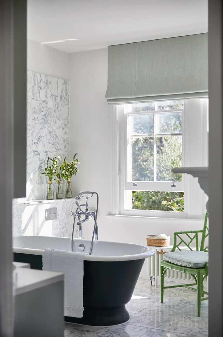 white bathroom with marble wall and floor, green chair, pale green blind, black painted roll top
