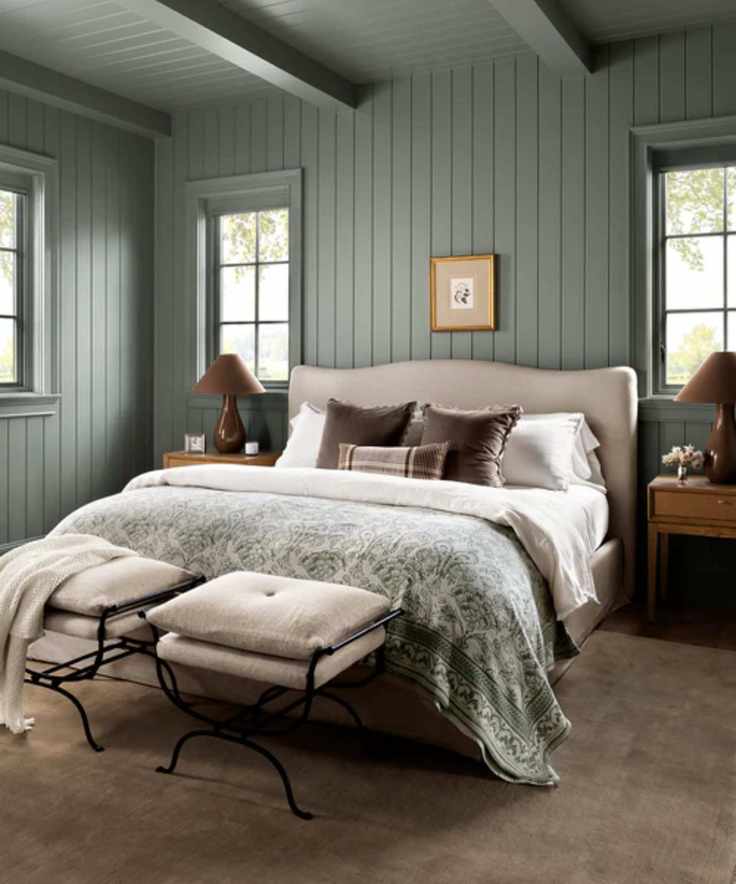 A serene blue-green bedroom featuring a neutral upholstered bed with wooden nightstands and two stylish ottomans at the foot