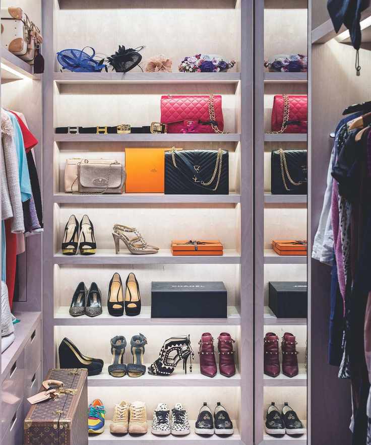 A walk-in closet with lit-up shelves filled with shoes, purses and clothes