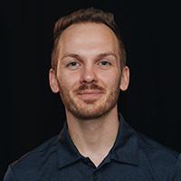 Headshot of Alex Panasyuk wearing a dark blue shirt against a black background.