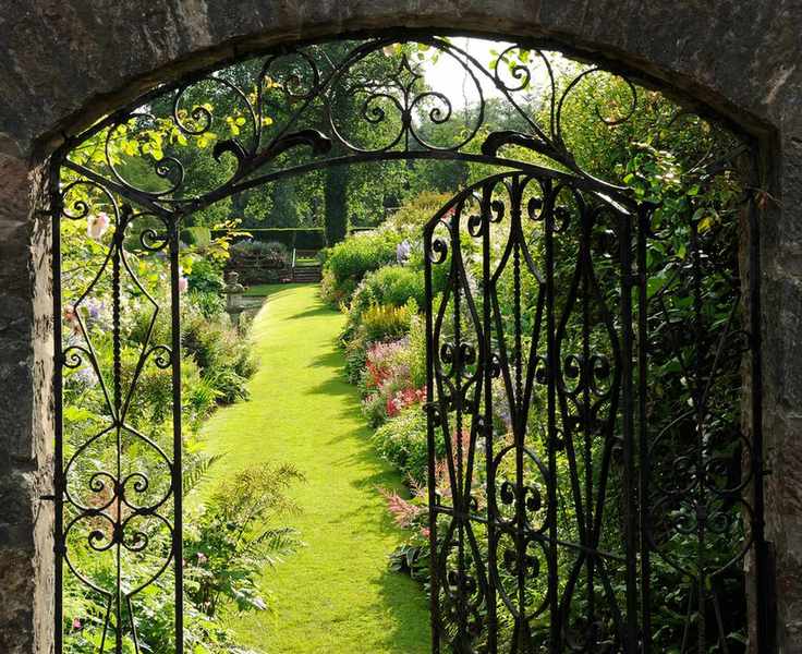 Bespoke ornate wrought iron garden gate in a stone wall, leading to formal bedding.