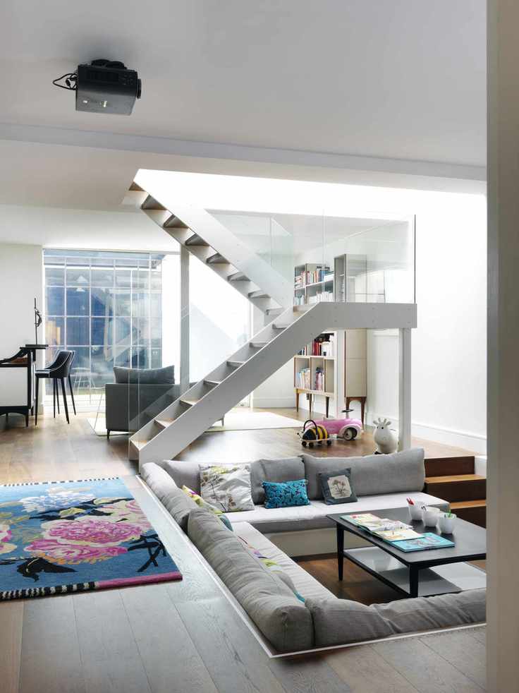 Basement with sunken seating area white staircase with clear baluster and floral rug on wood floor