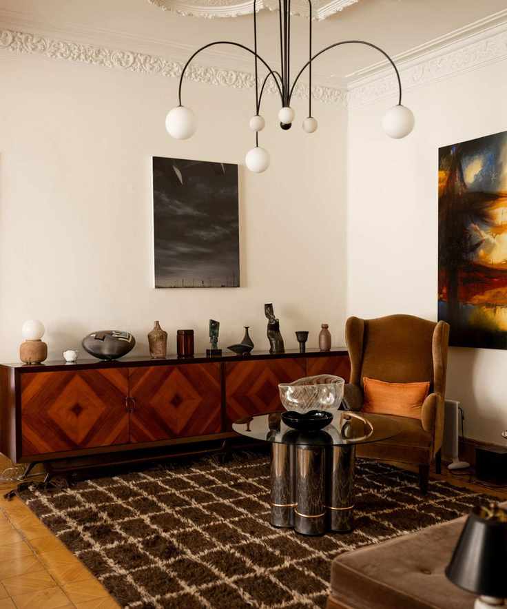 Contemporary living room with chequered rug, velvet armchair and wood cabinet holding a collection of ceramics and pottery