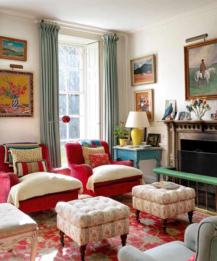 Charming country-style living room with matching red upholstered armchairs and ottomans, a large patterned rug, and colorful artwork on the walls.