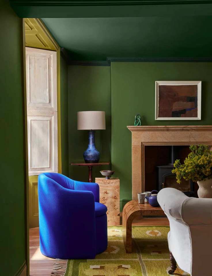 painted green living room with darker ceiling and a blue velvet armchair with a vintage rug
