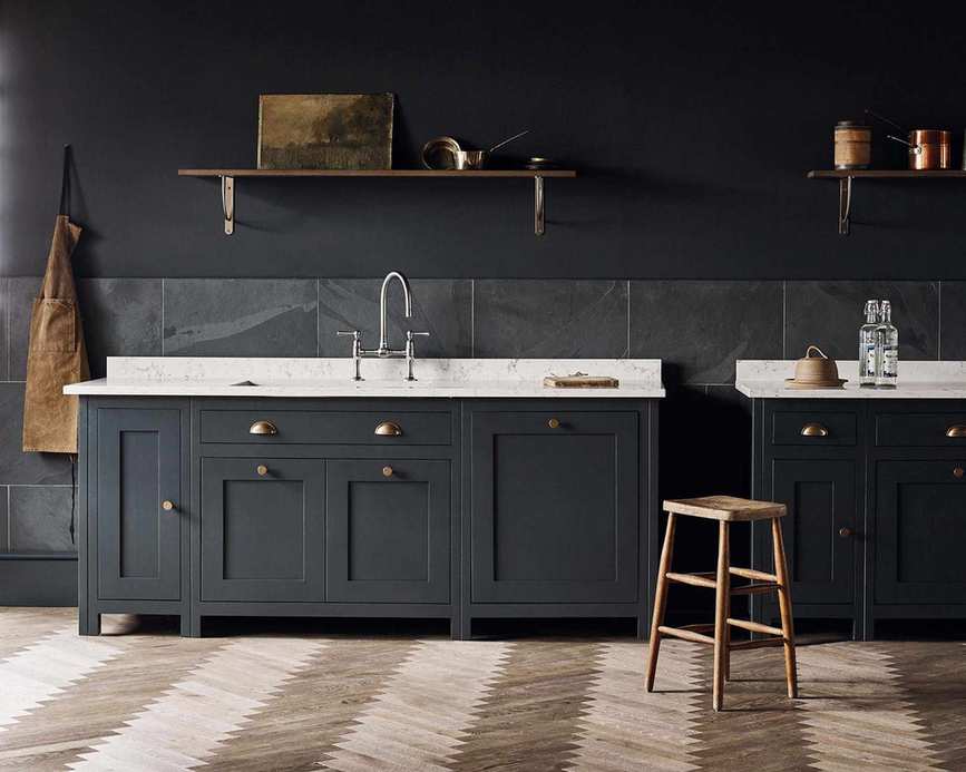 A black kitchen with herringbone flooring, white marble countertops and large-scale gray kitchen wall tiles.