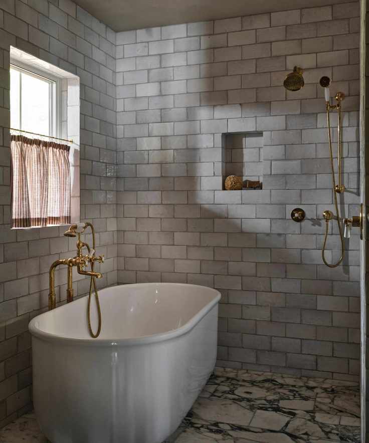 an earthy muted wet room bathroom with marble floor tiles, a free standing tub, subway zellige tiles on the walls and a small niche