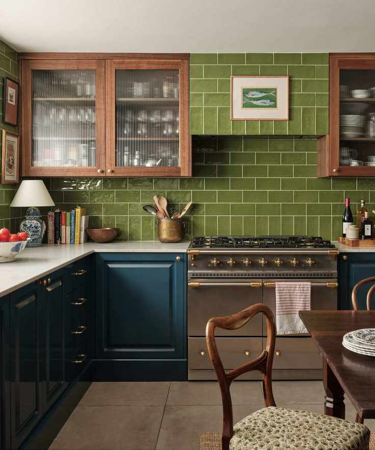 english kitchen with dark teal lower cabinets, upper glass fronted wooden cabinets, green tiled backsplash and cooker hood and silver range oven