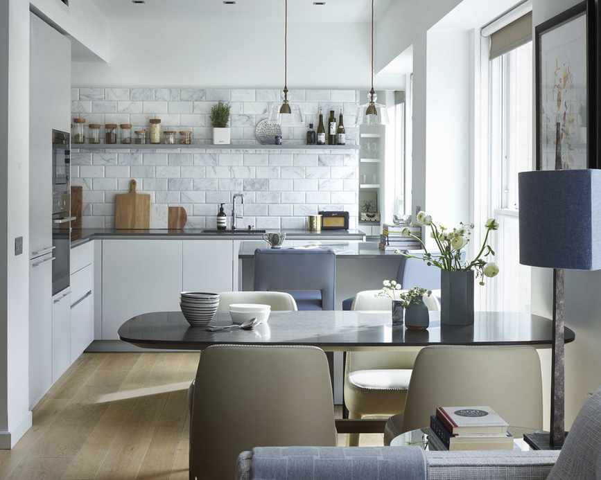 A white kitchen with a black dining table, blue and cream accents, featuring small white marble tiles as the backsplash.