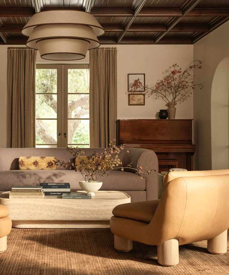 warm white living room styled for lulu and georgia fall 2025 with a beige rug, taupe drapes, a soft grey curved sofa and a tan leather arm chair