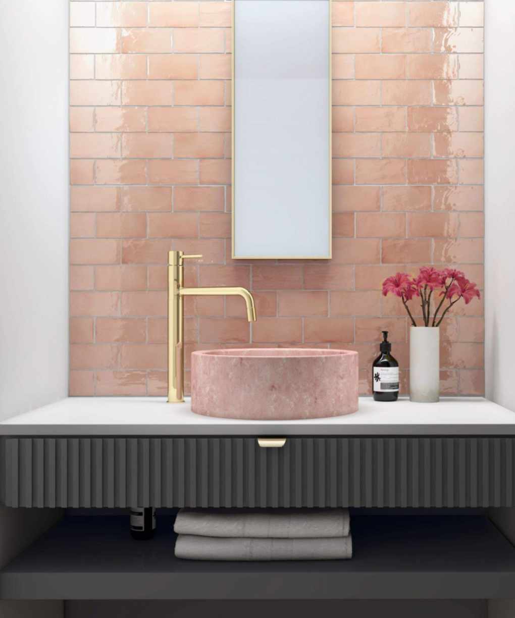 Tiled pink bathroom, featuring a pink basin, gold tap, and white countertop with a gold-rimmed mirror