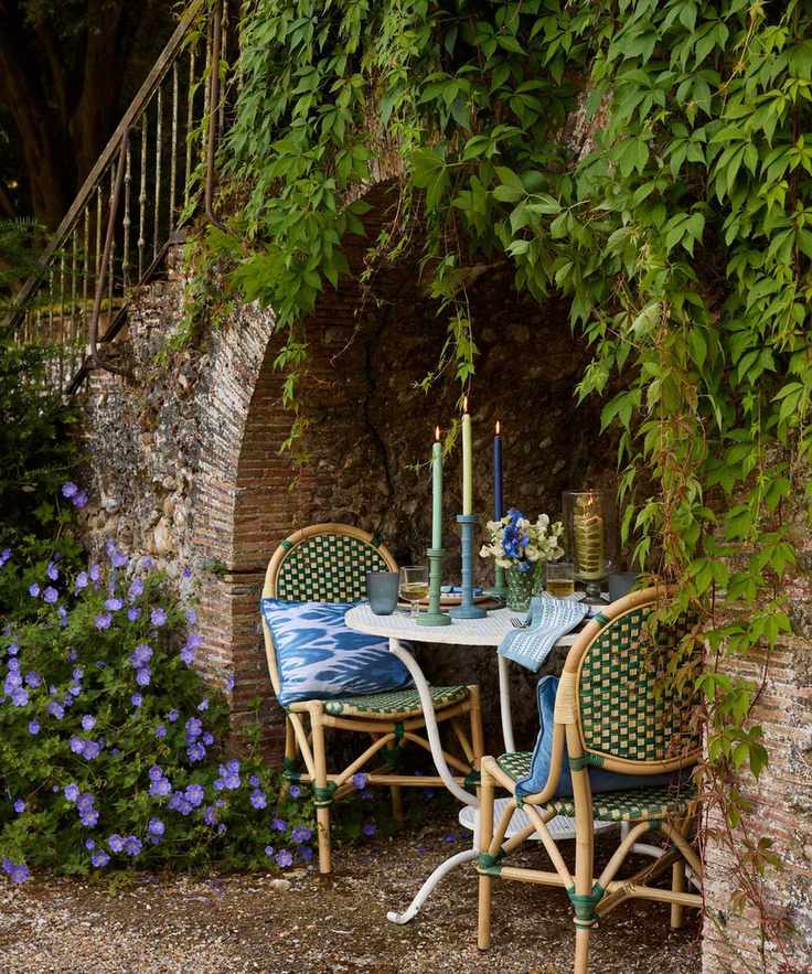 Outdoor bistro set for two for a romantic dinner in a stone wall nook with foliage and green rattan bamboo furniture