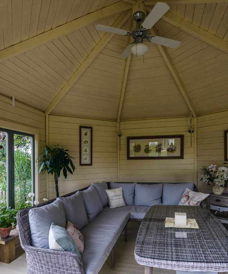 A sun room with a large L shaped rattan sofa and a ceiling fan