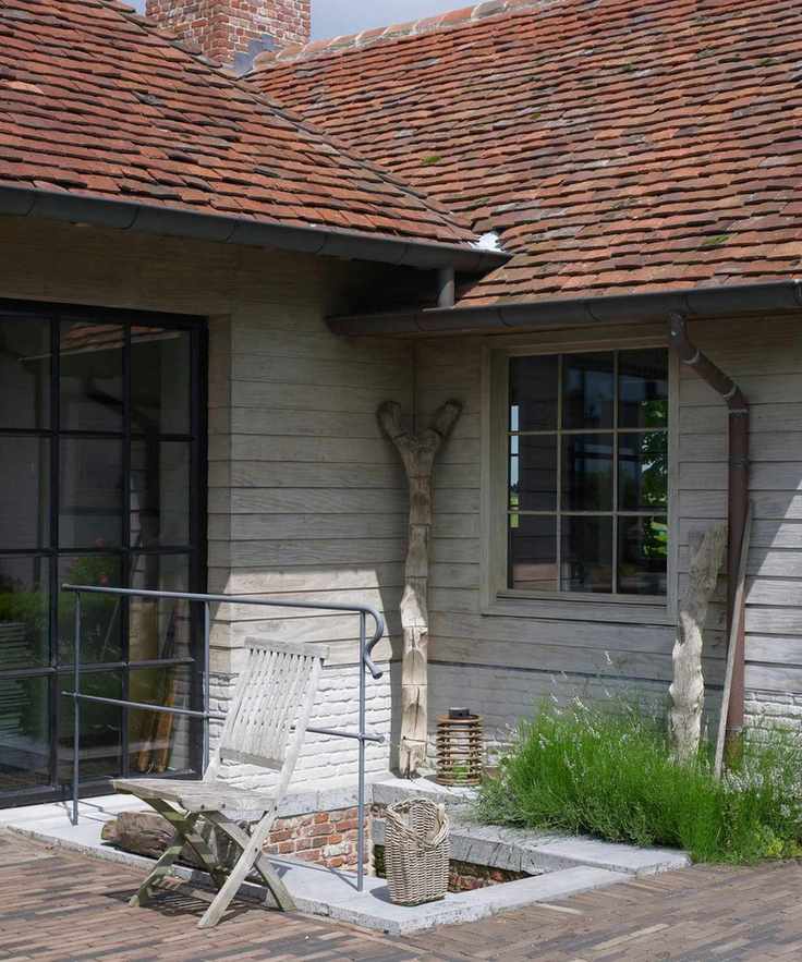 Exterior of a rustic farmhouse home with driftwood, panelled walls, a visible gutter and downspout, and patch of green grass