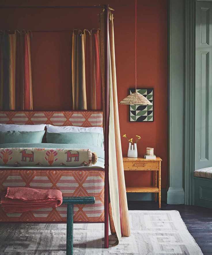 A burnt orange bedroom with sage green windows, an orange four-poster bed, and cream curtains
