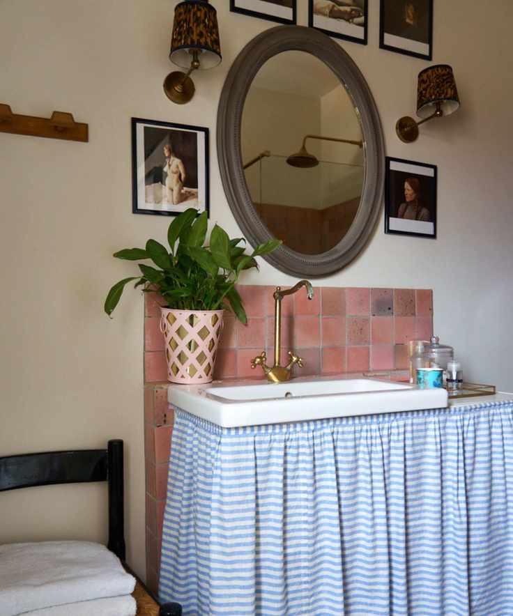 A small bathroom vanity with a blue and white striped cabinet skirt and pink square backsplash tiles