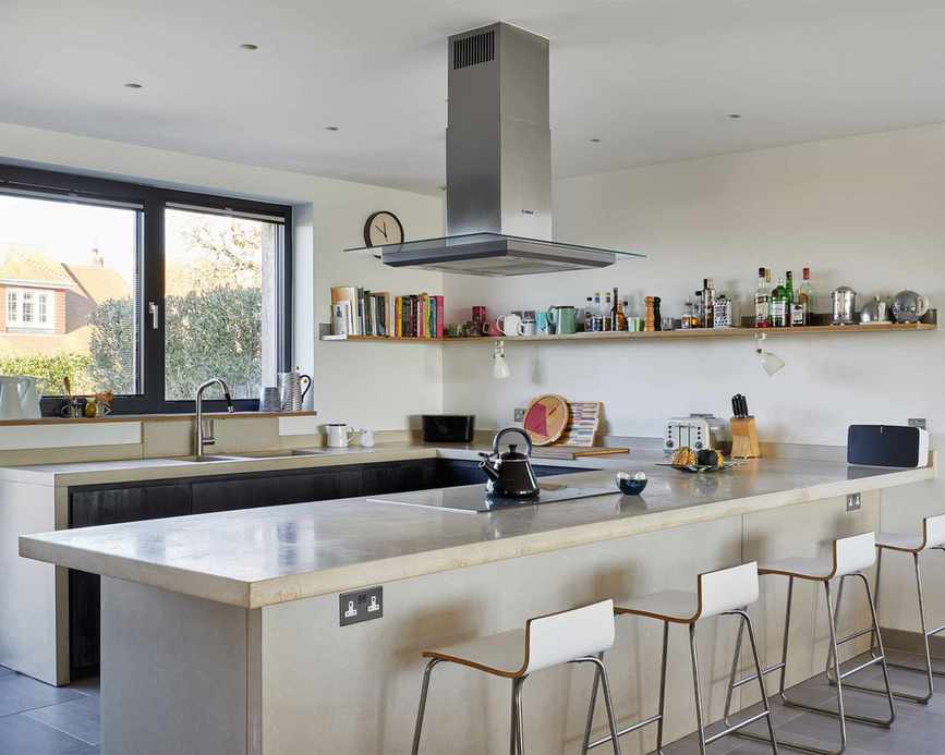 Kitchen with large limestone bar countertop, white wooden bar stools with metal frame, wall shelving decorated with books and ornaments