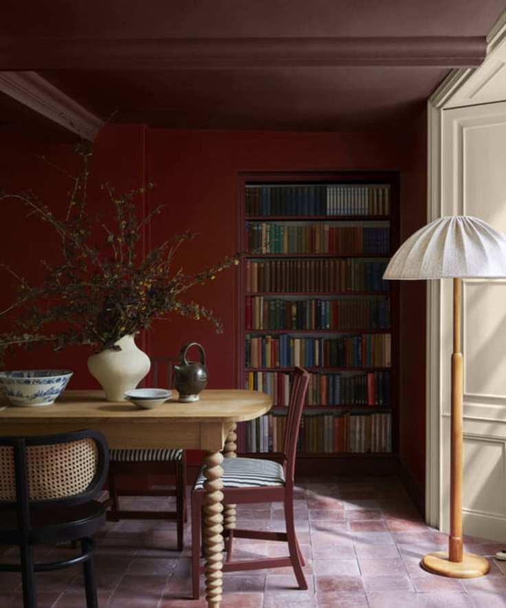 Color drenched red dining room with a wooden dining table and decorated with a vase of fall foliage and a wooden lamp with white shade