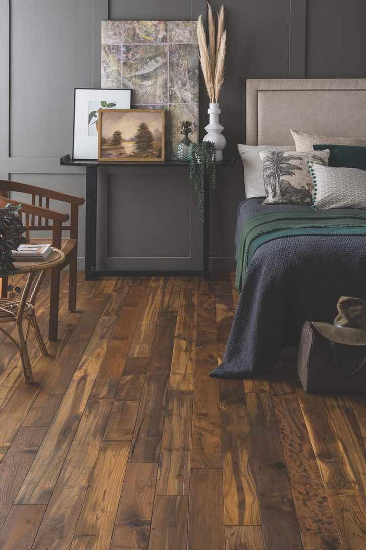Bedroom with bed and nightstand, side chair and table, grey paneled walls and dark wood floor