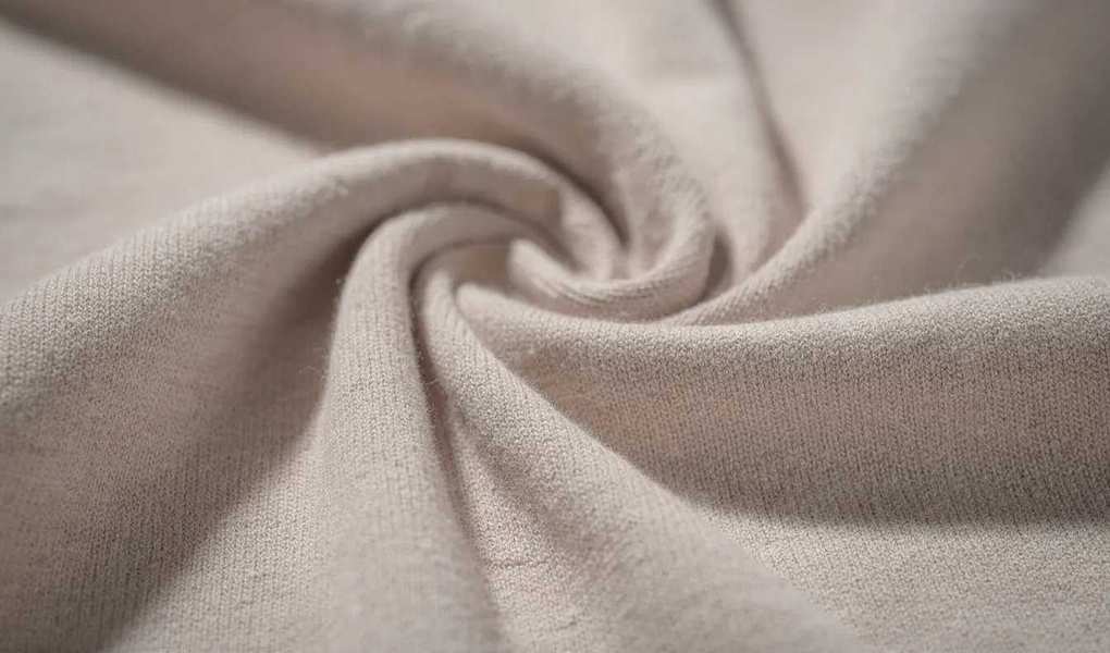 A close-up view of soft cotton jersey fabric in neutral tones, showcasing its gentle draping and luxurious texture, perfect for creating comfortable garments or apparel for your next project.