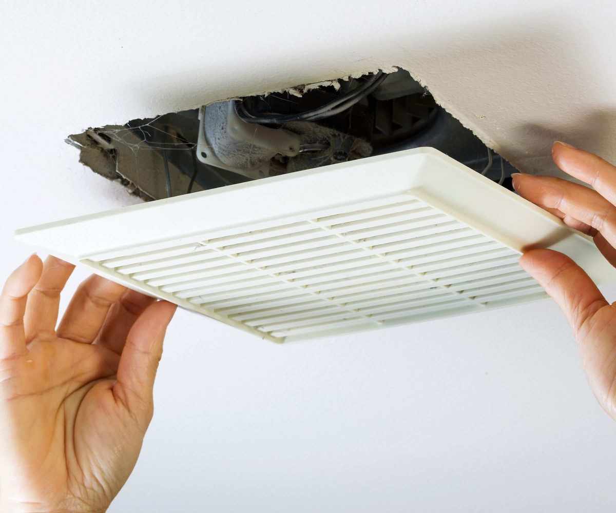 Close up horizontal photo of female hands removing bathroom fan vent cover from ceiling