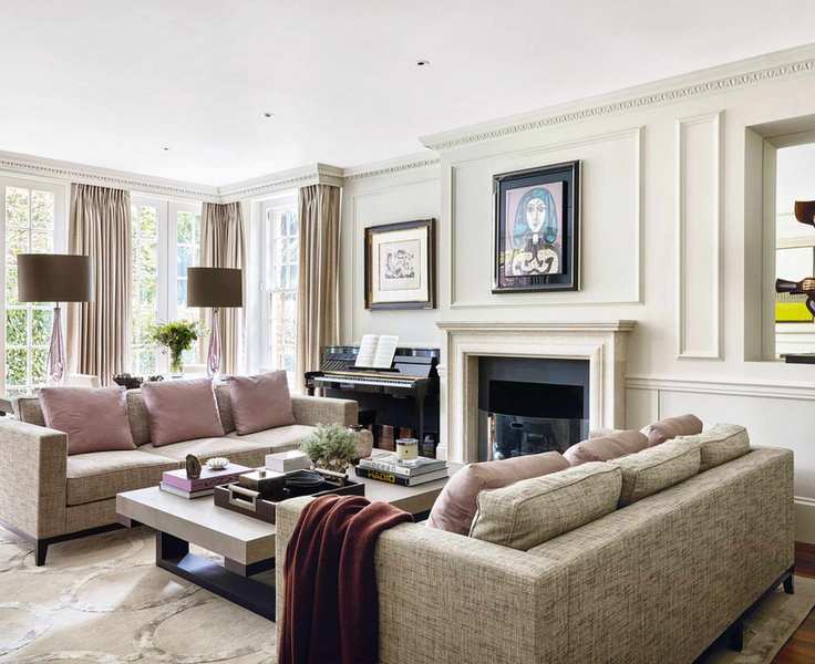 Bright living room with off white painted walls and paneling, spacious seating area with two gray three seater sofas, purple cushions, dark wood flooring with cream rug, twin gray table lamps, fireplace and piano