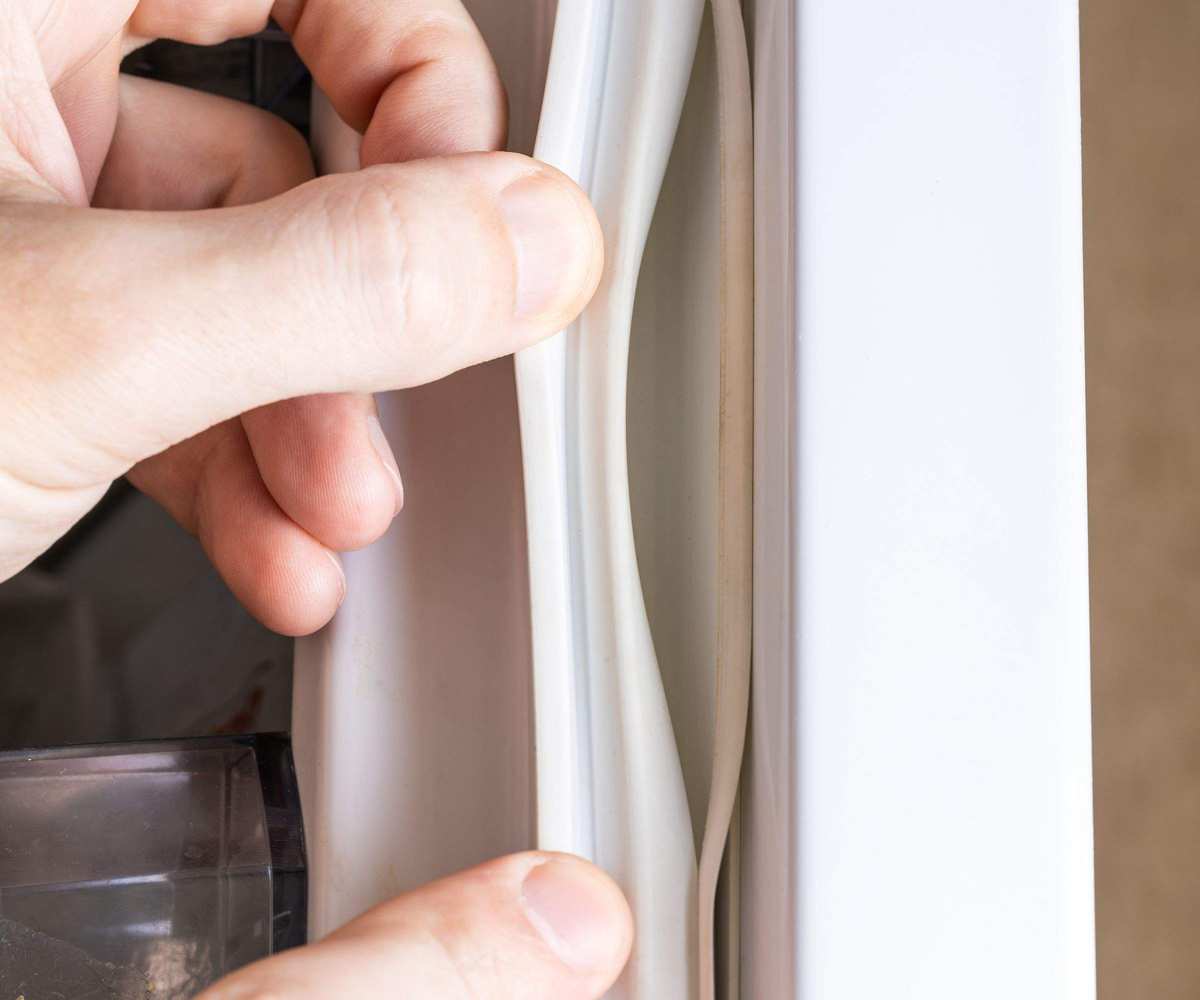 Someone pulling a broken white fridge door rubber seal away fromt the door. Close up