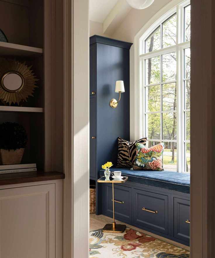 Sitting room with large arched window, blue cushion and drawers, small golden side table, and partial shot of bookshelf with circle mirror and magazines