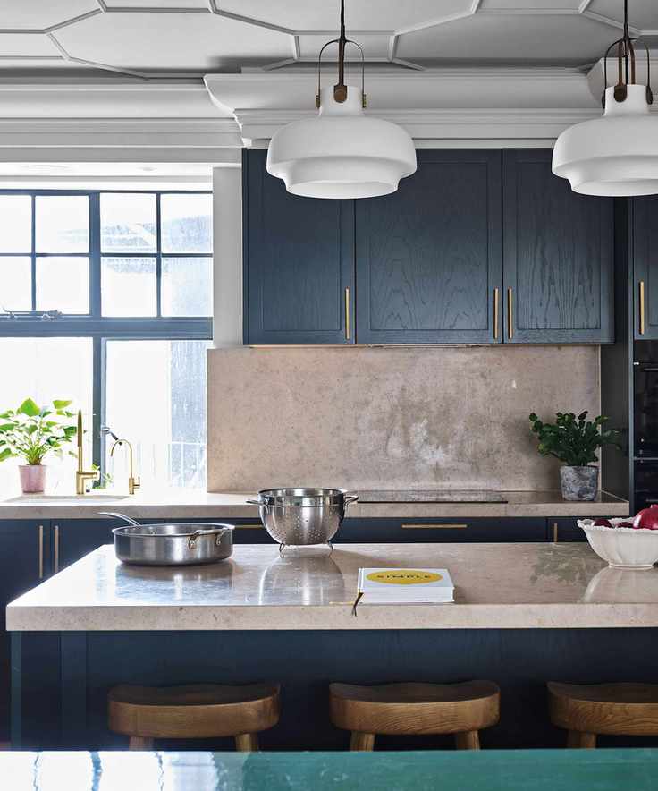 Kitchen island with pale granite polished stone worktop and dark grey units with brass handles.