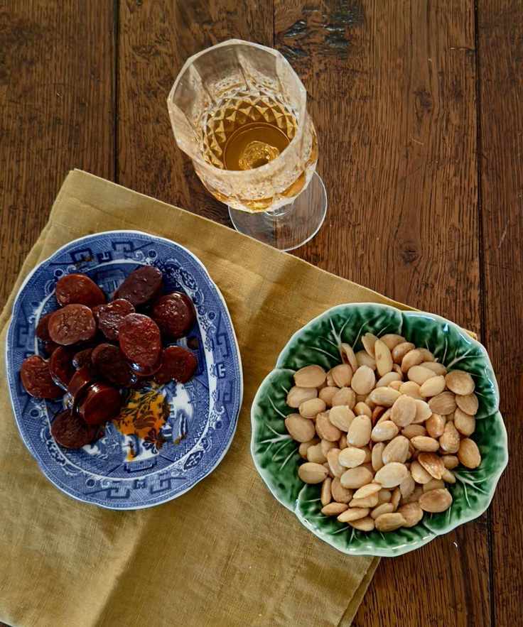 Bowl of sliced chorizo, nuts and a glass of sherry on a wooden table with a napkin