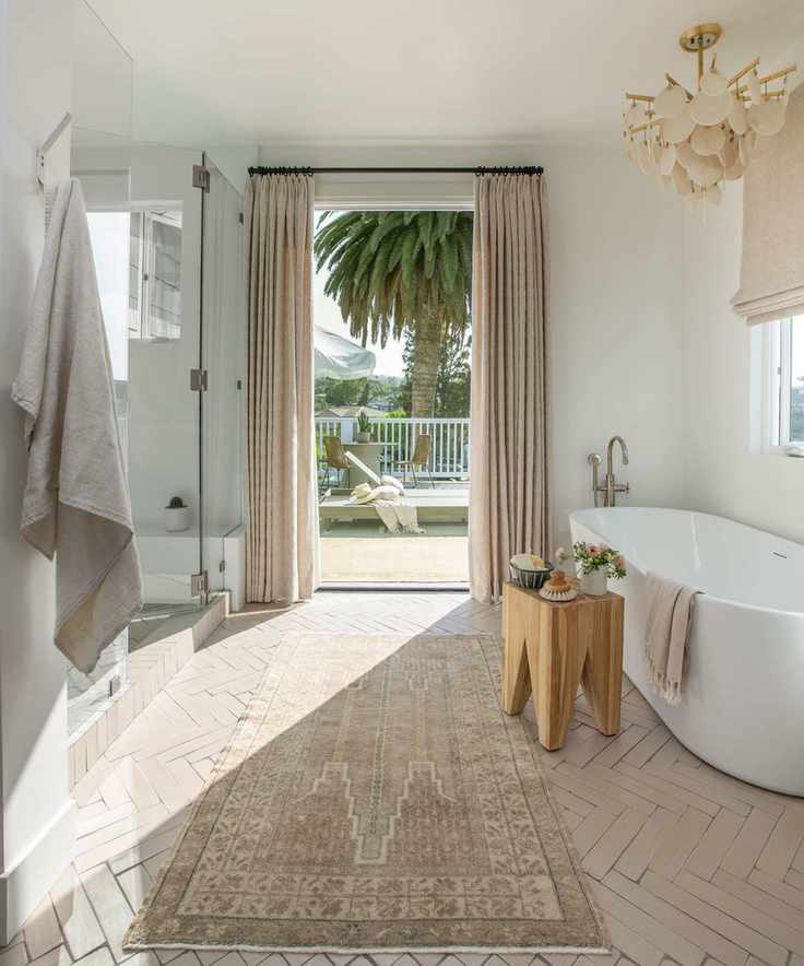 Neutral, calming bathroom with bathtub, rug, shower and open-doors looking out to the garden