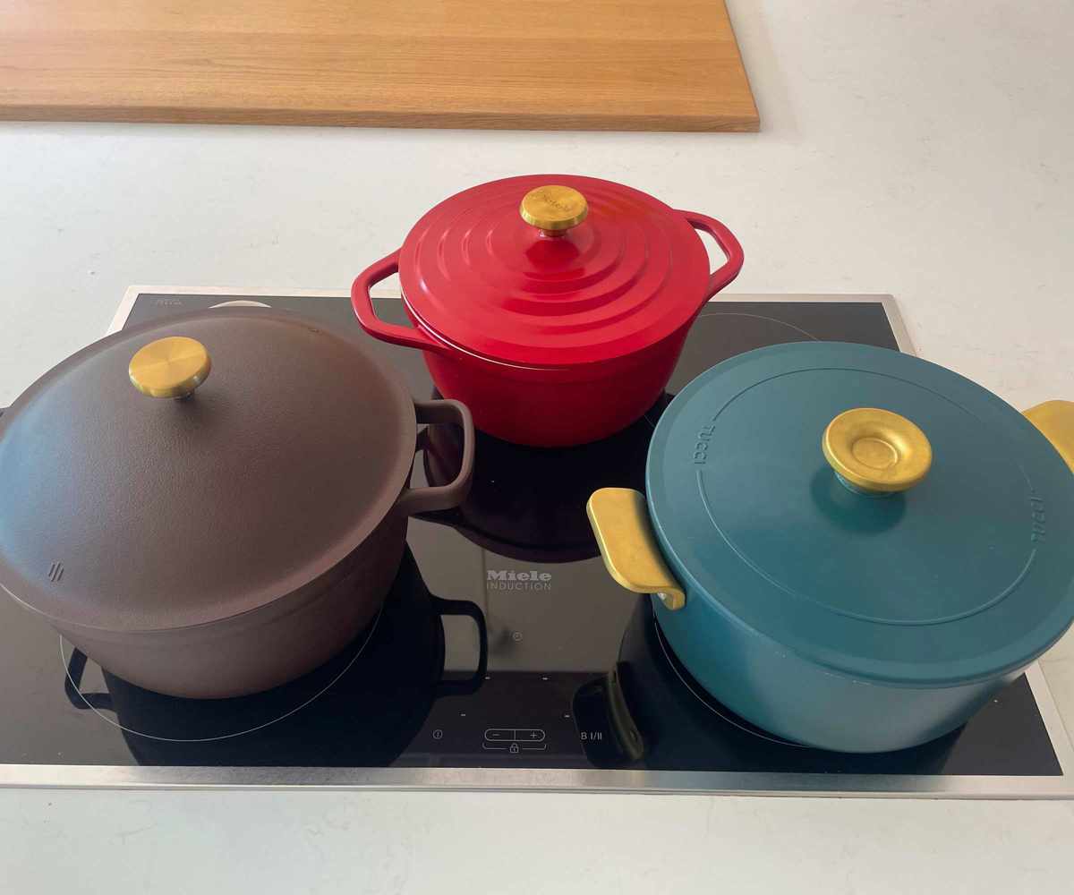 Purple, red, and blue Dutch ovens with gold knob lids on a black stovetop.
