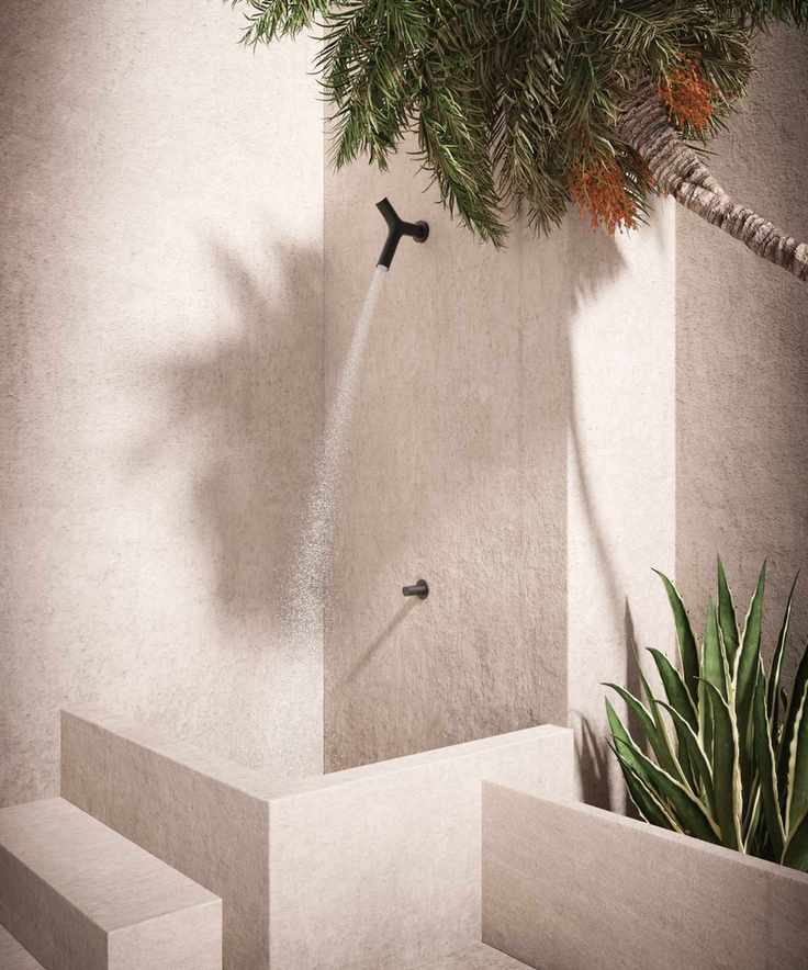 An outdoor shower with black, minimal hardware installed to a white cement wall
