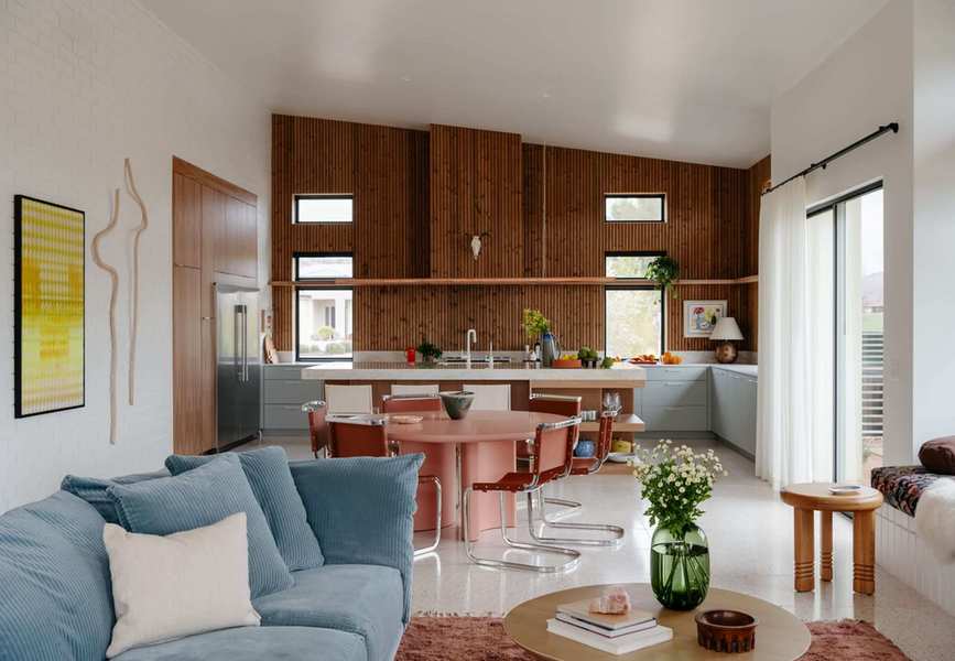 an open floor plan with a living room, a dining room with a rust-colored dining table, and a kitchen with wood paneled walls