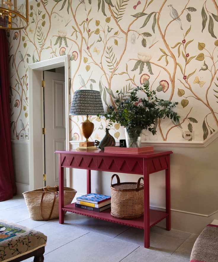 hallway with floral wallpaper above chair rail, stone painted underneath, red console and drapes, stone floor tiles, lamp, baskets, runner on stairs, Georgie Wykeham Designs