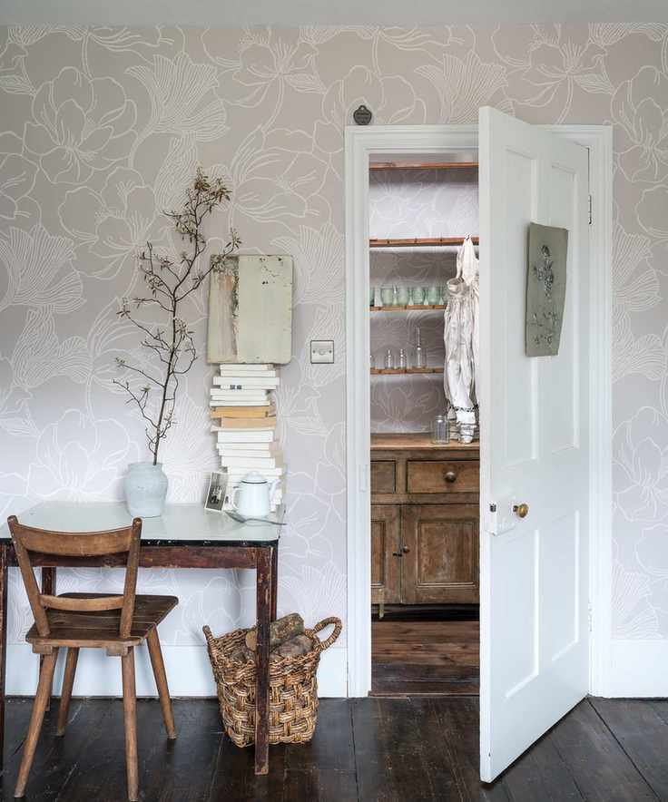 How to wallpaper a room, with pale beige patterned paper in a white room with wooden floorboards and a small desk beside an open door.