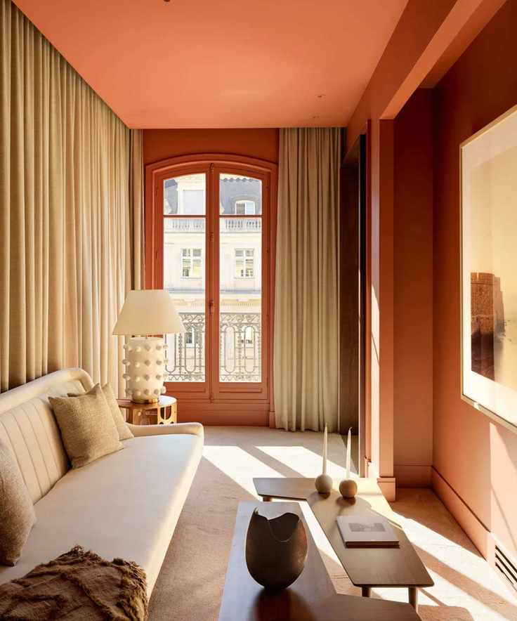 a room with an orange ceiling, curtains on the walls, a cream colored couch, and a wooden abstract coffee table