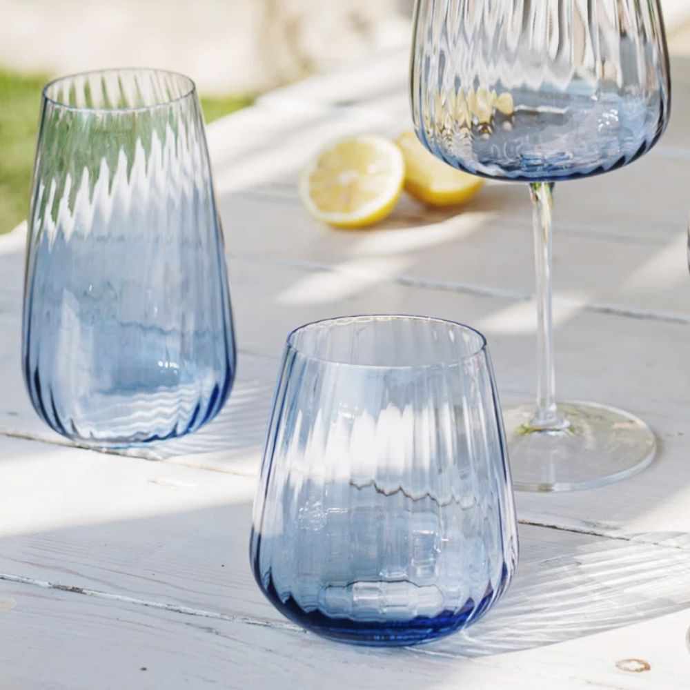 three blue glasses on a white wooden table with cut lemons in the background
